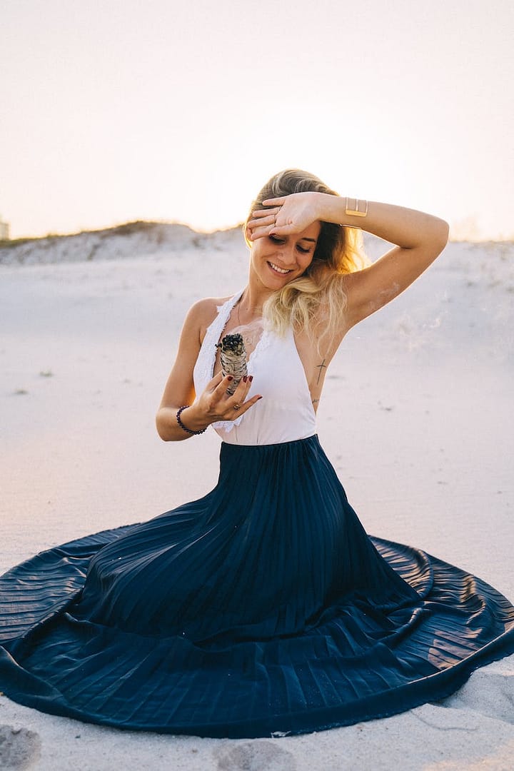 a smiling woman holding a burning white sage